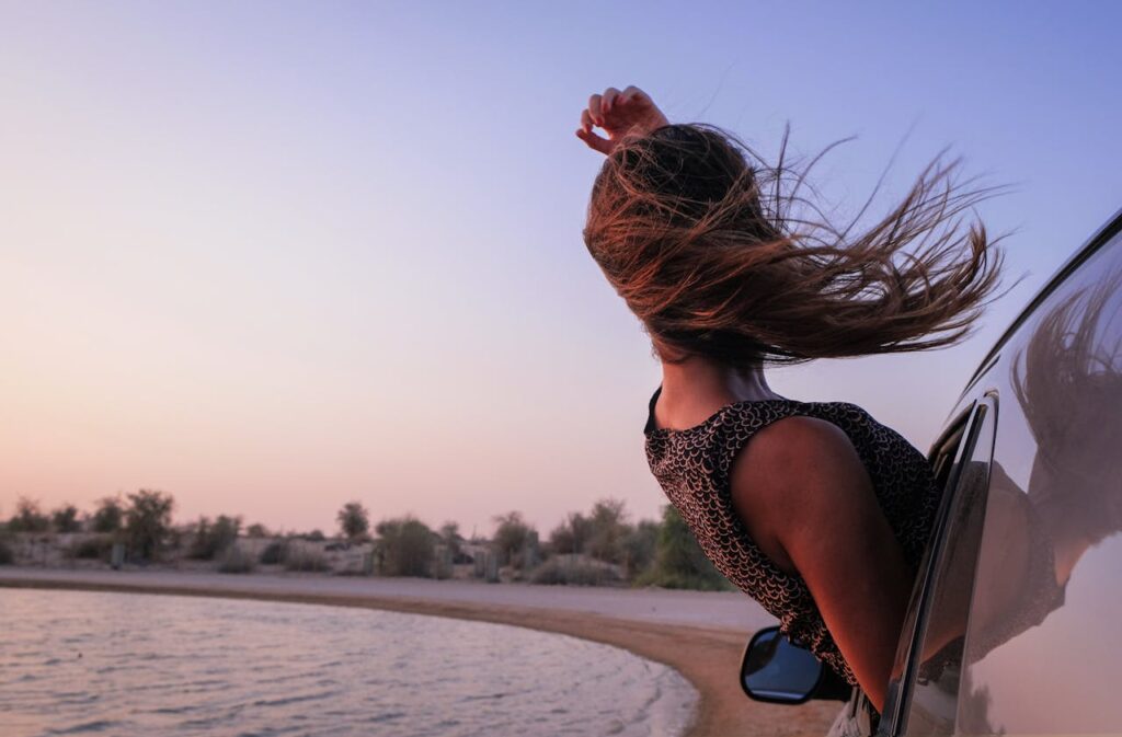 pexels photo 1170345 A young woman enjoys the sunset view from a car window during a beach roadtrip in Dubai.