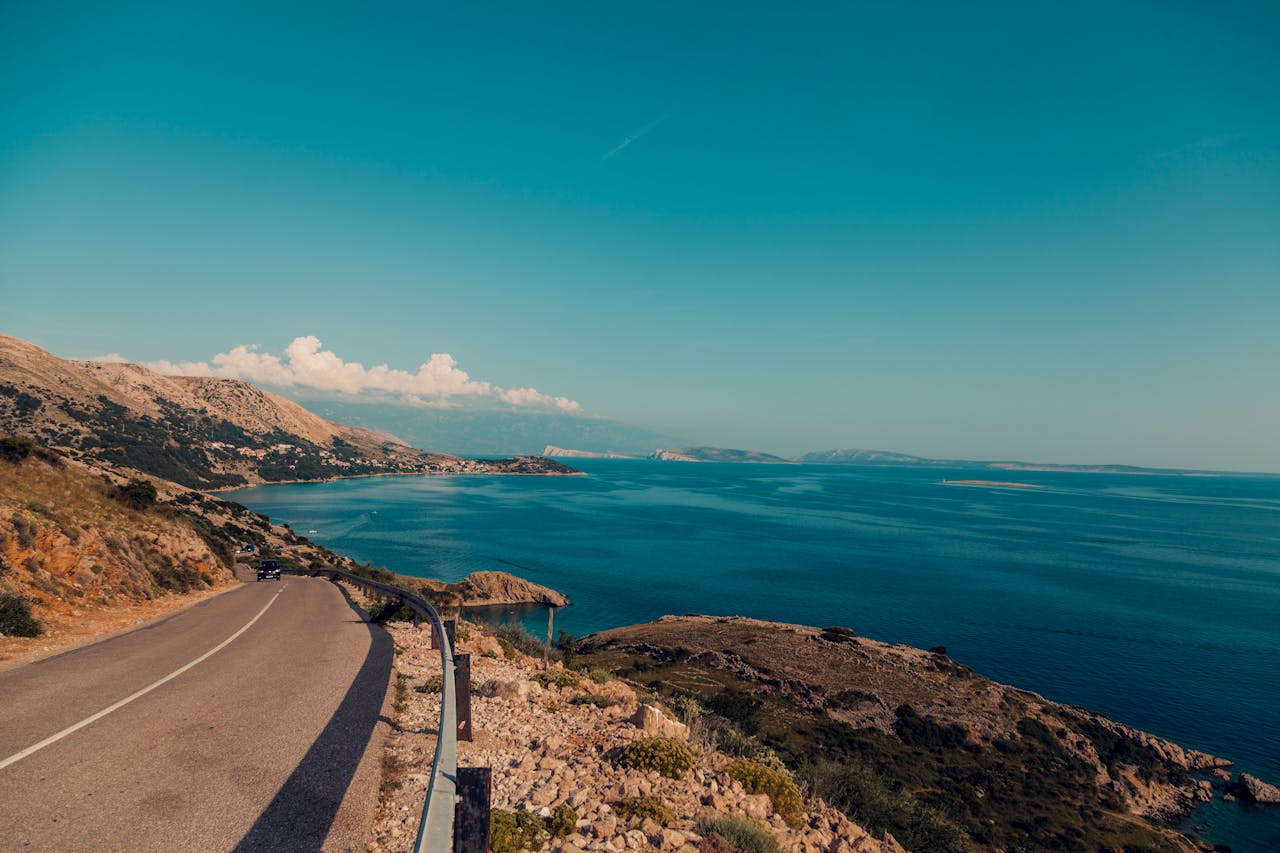 services-02 Breathtaking view of a coastal road alongside the ocean with clear blue skies and rugged terrain.