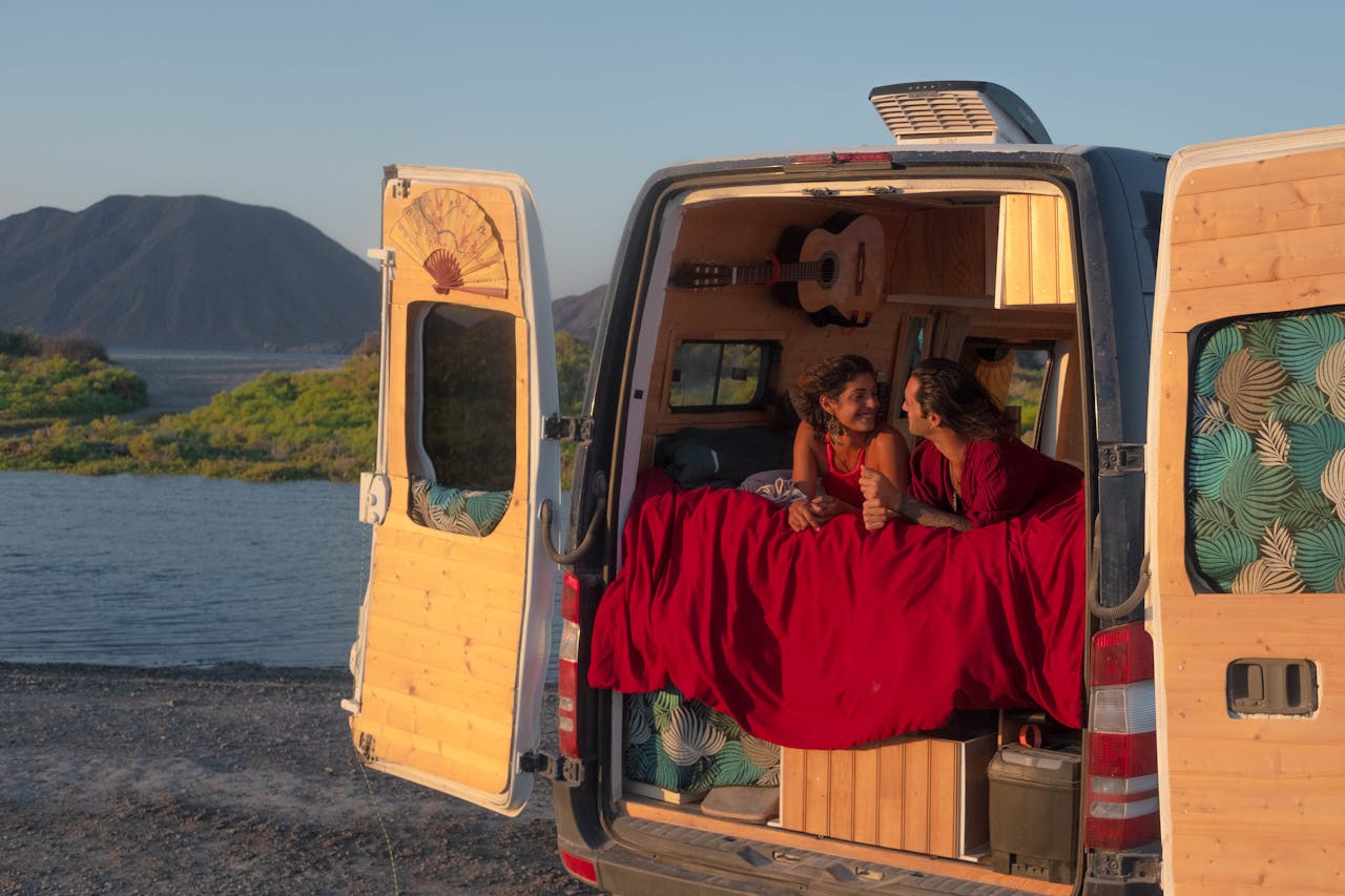 Couple relaxing in camper van by a scenic lake, embracing travel and nature.