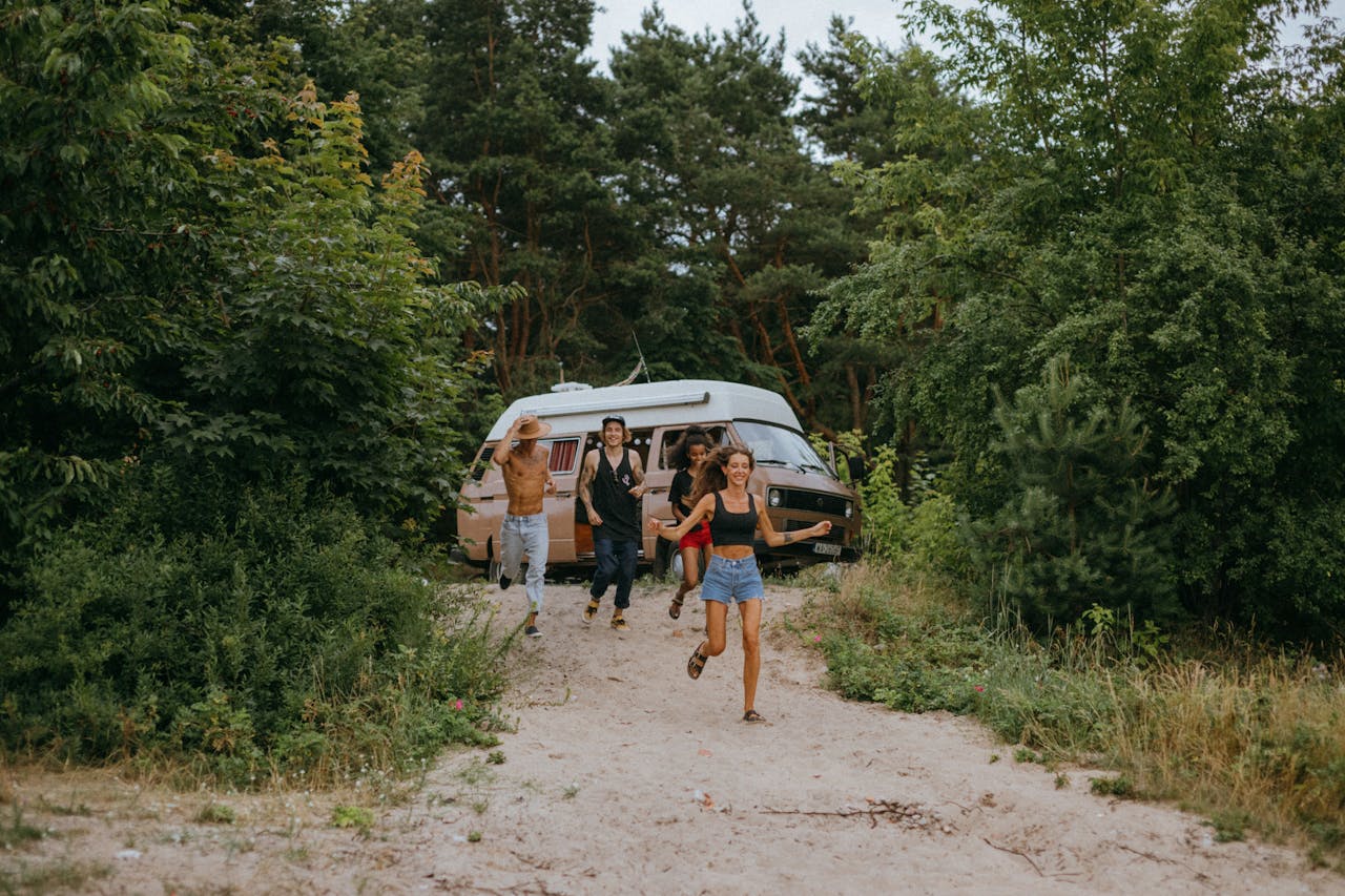 services-02 Group of friends running joyfully from a camper van in a lush forest setting during summer.