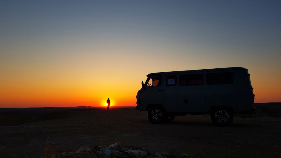 A van and person silhouetted against a colorful sunset in Mongolia, capturing a serene travel moment.